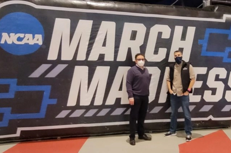 two people wearing masks in front of march madness sign